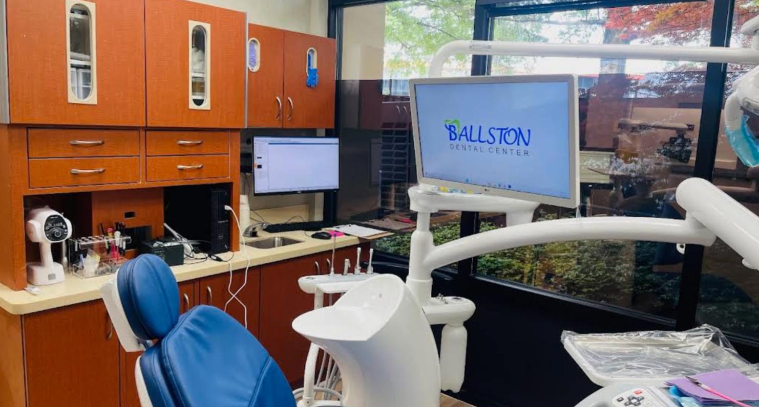 The image shows a dental office interior with a modern dental chair, a computer monitor displaying Ballston Dental, and various dental equipment in the background.