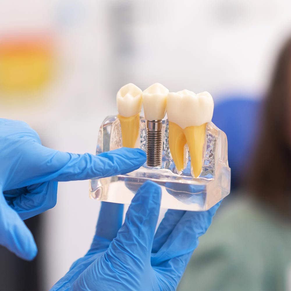 The image shows a dental hygiene professional holding up a transparent display containing a toothbrush, dental floss, and a dental pick for demonstration purposes, with a focus on oral health care tools.