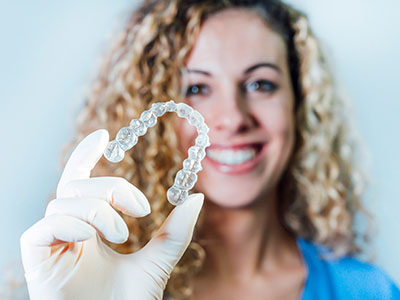 Woman holding up a clear plastic bracelet with a smile, set against white background.