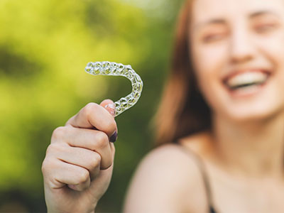 A person holding up a clear plastic object with a smile, possibly indicating dental health or orthodontic appliance.