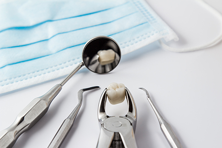 The image displays a collection of dental instruments, including a toothbrush with a bristle, placed on a white background, with a blue surgical mask in the foreground.