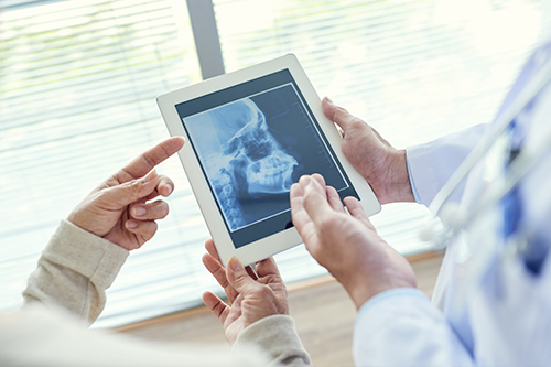 The image depicts two individuals interacting with a tablet displaying an X-ray image, with a medical professional pointing at it while another person holds the device.