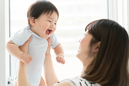 A woman holds a baby who is smiling and clapping their hands while looking up at the camera.