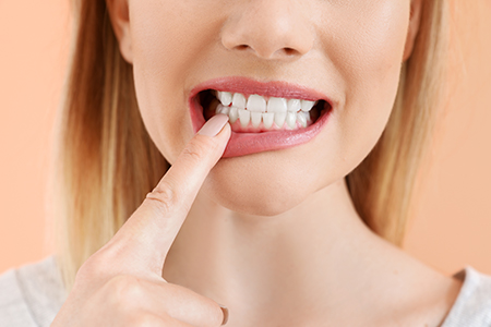 A woman with a toothbrush in her mouth, holding up a finger, against a blurred background.