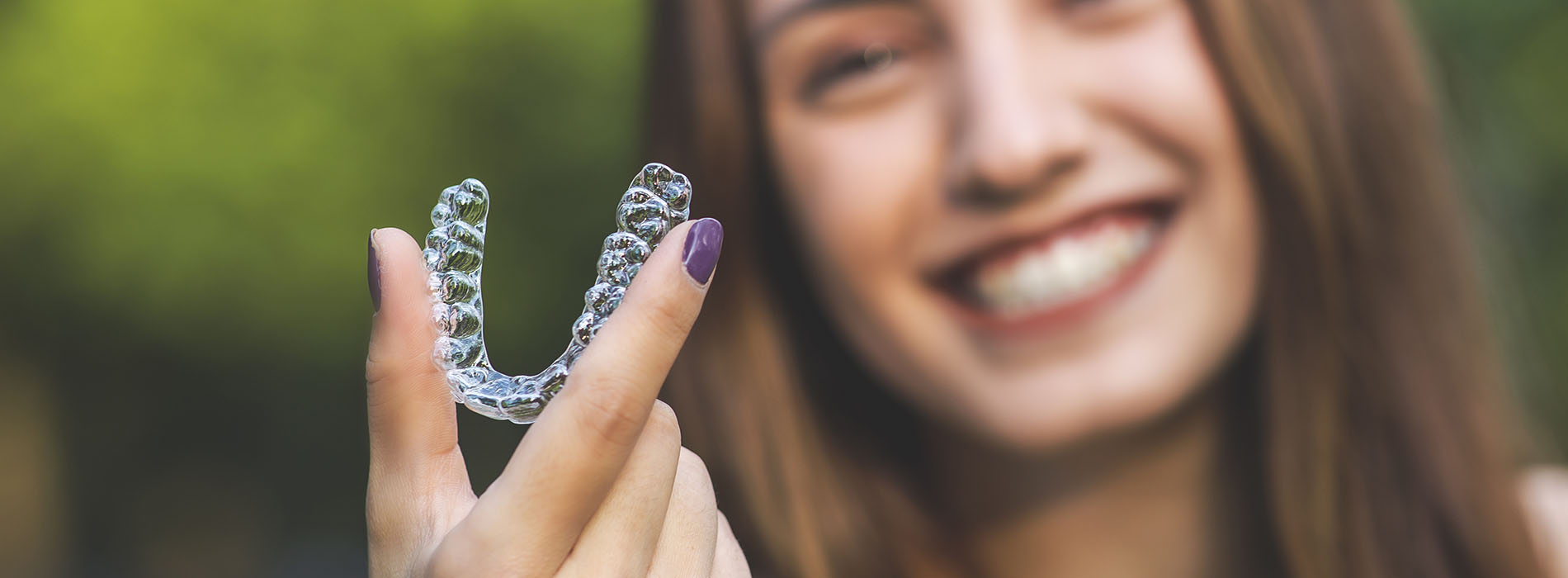 This is a photograph of a smiling woman holding up a transparent plastic sheet with a letter V embossed on it, which appears to be a watermark or logo.